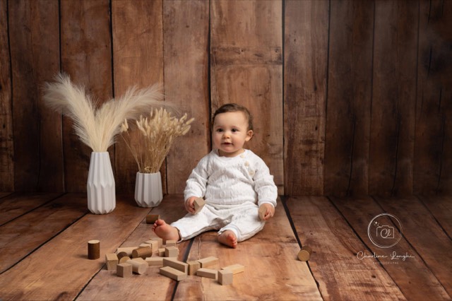 Séance photo bébé assis avec sol et fond photo en imitation parquet en bois marrons foncé, fleurs séchées et cube en bois