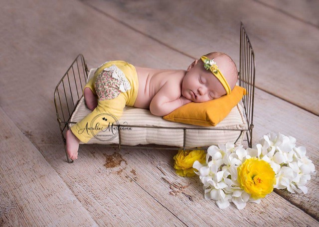 séance photo nouveau-né sur petit lit et coussin jaune, sol photo imitation plancher en bois beige