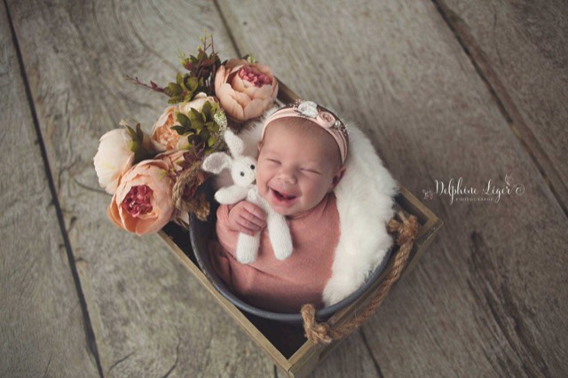 Séance photo nouveau-né, bébé sourianr emmailloté dans tissu rose sur sol en bois imitation plancher gris, Fond photo